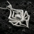 Load image into Gallery viewer, Polished silver spider necklace with detailed leg texture, realistic body form, and striking animal-inspired design placed on textured volcanic rock in a premium studio product shot