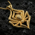 Load image into Gallery viewer, Gold plated spider pendant with sculpted arachnid body, textured leg detailing, and bold gothic silhouette showcased on black volcanic rock in a refined macro jewelry image