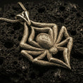 Load image into Gallery viewer, Bronze spider pendant with textured legs, sculpted body relief, and bold arachnid silhouette displayed on dark volcanic rock in a close-up luxury jewelry composition