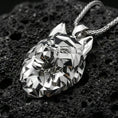 Load image into Gallery viewer, Polished silver geometric wolf necklace with faceted low poly wolf face, sharp angular contours, and modern animal head design placed on textured volcanic rock in a premium studio product shot
