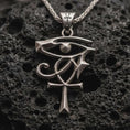 Load image into Gallery viewer, Sterling silver Eye of Ra and Ankh pendant necklace with an oxidized finish resting on textured volcanic rock, captured in a close-up premium studio composition.