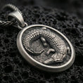 Load image into Gallery viewer, Sterling silver crocodile pendant necklace with an oxidized finish resting on textured volcanic rock, shown in a close-up premium studio composition.