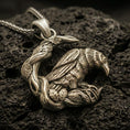 Load image into Gallery viewer, Bronze Viking raven pendant necklace with an oxidized finish displayed on textured volcanic rock in a dramatic close-up studio composition.