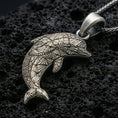 Load image into Gallery viewer, Sterling silver dolphin pendant necklace with an oxidized finish resting on textured volcanic rock, captured in a close-up premium studio composition.