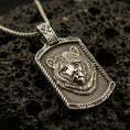 Load image into Gallery viewer, Bronze bear pendant necklace with an oxidized finish resting on textured volcanic rock, captured in a close-up premium studio composition.