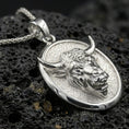Load image into Gallery viewer, Polished silver bull pendant necklace displayed on black volcanic rock, shown in a refined macro product shot with sculpted horn and facial detail.