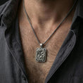 Load image into Gallery viewer, Oxidized cobra pendant necklace worn on the neck, styled in a dark lifestyle portrait with an open shirt and masculine presentation.