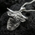 Load image into Gallery viewer, Polished silver buffalo head pendant necklace displayed on black volcanic rock, shown in a refined macro product shot with detailed horn and fur sculpting.