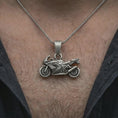 Load image into Gallery viewer, Oxidized sportbike motorcycle pendant necklace worn on the neck, styled in a dark lifestyle portrait with an open shirt and masculine presentation.