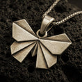Load image into Gallery viewer, Bronze origami butterfly pendant necklace with an oxidized finish resting on textured volcanic rock, captured in a close-up premium studio composition.