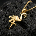 Load image into Gallery viewer, Gold plated origami flamingo pendant necklace presented on porous volcanic rock, highlighting the angular bird silhouette in a luxurious close-up jewelry image.