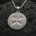 Load image into Gallery viewer, Polished silver Celtic knot medallion necklace displayed on black volcanic rock, shown in a refined macro product shot with intricate Gaelic weave and circular symbolic relief.