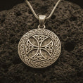 Load image into Gallery viewer, Bronze Celtic knot medallion necklace with an oxidized finish resting on textured volcanic rock, captured in a close-up premium studio composition.
