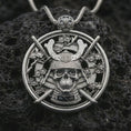 Load image into Gallery viewer, Polished silver samurai skull pendant necklace displayed on black volcanic rock, shown in a refined macro product shot with katana swords, floral accents, and armored helmet detail.