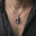 Load image into Gallery viewer, Oxidized Mythosaur skull pendant necklace worn on the neck, styled in a dark lifestyle portrait with an open shirt and masculine presentation.