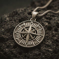 Load image into Gallery viewer, Bronze compass rose pendant necklace with an oxidized finish resting on textured volcanic rock, captured in a close-up premium studio composition.