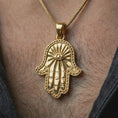 Load image into Gallery viewer, Gold plated Hamsa hand pendant necklace worn on the neck, captured on a human model in a premium dark-toned lifestyle frame.