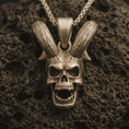 Load image into Gallery viewer, Bronze rabbit skull pendant necklace with an oxidized finish resting on textured volcanic rock, captured in a close-up premium studio composition.