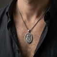 Load image into Gallery viewer, Oxidized Saint Patrick pendant necklace worn on the neck, styled in a dark lifestyle portrait with an open shirt and masculine presentation.