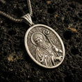 Load image into Gallery viewer, Bronze Saint Patrick pendant necklace with an oxidized finish resting on textured volcanic rock, captured in a close-up premium studio composition.