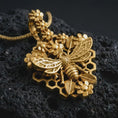 Load image into Gallery viewer, Gold plated floral bee pendant necklace presented on porous volcanic rock, highlighting the nature-inspired honeybee and blossom motif in a luxurious close-up jewelry image.