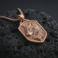 Load image into Gallery viewer, Rose gold plated wolf shield pendant necklace on dark volcanic rock, photographed in a detailed premium studio macro view.