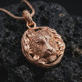 Load image into Gallery viewer, A rose gold plated tiger pendant on volcanic rock with warm tone emphasizing the wreath texture and deep stripe engraving.