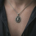 Load image into Gallery viewer, Oxidized ram head pendant necklace worn on the neck, styled in a dark lifestyle portrait with an open shirt and strong symbolic presentation.