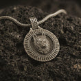 Load image into Gallery viewer, Bronze Fenrir wolf pendant necklace with an oxidized finish resting on textured volcanic rock, captured in a close-up premium studio composition.