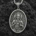 Load image into Gallery viewer, Sterling silver Jesus Christ pendant necklace with an oxidized finish resting on textured volcanic rock, captured in a close-up premium studio composition.