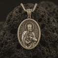 Load image into Gallery viewer, Bronze Saint Peter pendant necklace with an oxidized finish resting on textured volcanic rock, captured in a close-up premium studio composition.