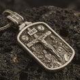 Load image into Gallery viewer, Bronze Jesus INRI crucifixion pendant necklace with an oxidized finish resting on textured volcanic rock, captured in a close-up premium studio composition.
