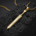 Load image into Gallery viewer, Gold plated Dragonslayer sword pendant necklace presented on porous volcanic rock, highlighting the oversized sword silhouette in a luxurious close-up jewelry image.