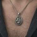 Load image into Gallery viewer, Oxidized wolf medallion pendant necklace worn on the neck, styled in a dark lifestyle portrait with an open shirt and bold nature-inspired presentation.