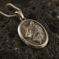 Load image into Gallery viewer, Bronze wolf medallion pendant necklace with an oxidized finish resting on textured volcanic rock, captured in a close-up premium studio composition.