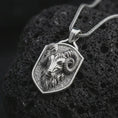 Load image into Gallery viewer, Polished silver ram head shield pendant necklace displayed on black volcanic rock, shown in a refined macro product shot with curled horns, sculpted Aries face detail, and angular shield frame.