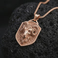 Load image into Gallery viewer, Rose gold plated ram head shield pendant necklace on dark volcanic rock, photographed in a detailed premium studio macro view.