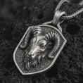 Load image into Gallery viewer, Ram head shield pendant necklace in oxidized sterling silver resting on black volcanic stone, shown in a detailed macro product photograph with curved horns and a textured shield frame.