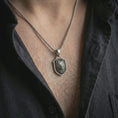 Load image into Gallery viewer, Wolf shield pendant necklace in oxidized sterling silver worn on the neck, styled in a dark lifestyle shot that emphasizes the fierce animal design against the chest.