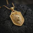 Load image into Gallery viewer, Wolf shield pendant necklace with a gold plated finish placed on porous volcanic stone, photographed in a refined macro composition with strong predator detail and symbolic warrior styling.