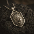 Load image into Gallery viewer, Wolf shield pendant necklace in oxidized Bronze resting on black volcanic stone, shown in a detailed macro product photograph with textured fur, alert ears, and an angular shield frame.