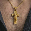 Load image into Gallery viewer, Gold plated symbolic cross pendant worn on the neck, captured on a human model in a premium dark-toned lifestyle frame.
