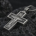 Load image into Gallery viewer, Sterling silver Cristo Protetor cross pendant necklace with an oxidized finish resting on textured volcanic rock, captured in a close-up premium studio composition.
