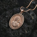 Load image into Gallery viewer, Rose gold plated Madonna and Child pendant necklace presented on porous volcanic stone, showcasing the layered oval frame and tender holy mother and child relief in a luxury macro image.