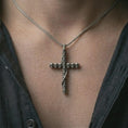 Load image into Gallery viewer, Oxidized skull cross pendant necklace worn on the neck, styled in a dark lifestyle portrait with an open shirt and masculine presentation.