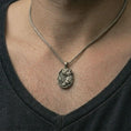 Load image into Gallery viewer, Oxidized howling wolf pendant necklace worn on the neck, styled in a dark lifestyle portrait with an open shirt and masculine presentation.
