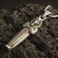 Load image into Gallery viewer, Bronze King Tut pendant necklace with an oxidized finish resting on textured volcanic rock, captured in a close-up premium studio composition.