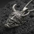 Load image into Gallery viewer, Sterling silver Oni mask pendant necklace with an oxidized finish resting on textured volcanic rock, captured in a close-up premium studio composition.