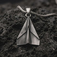Load image into Gallery viewer, Sterling silver origami airplane pendant necklace with an oxidized finish resting on textured volcanic rock, captured in a close-up premium studio composition.