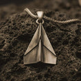 Load image into Gallery viewer, Bronze origami airplane pendant necklace with an oxidized finish resting on textured volcanic rock, captured in a close-up premium studio composition.